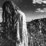 Long-haired person standing in a black and white field.